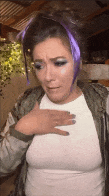 a woman with purple hair and a white shirt is holding her chest