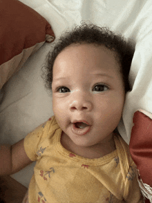 a baby laying on a bed with a yellow shirt on