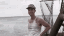 a man wearing a hat and a tank top is standing on a boat in the ocean .