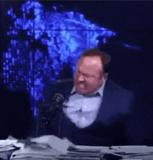 a man in a suit and tie is sitting at a table with a microphone .