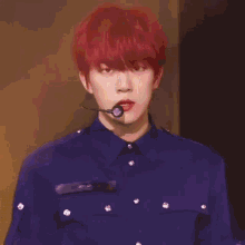 a young man with red hair and a microphone in his mouth is wearing a blue shirt .