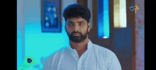 a man with a beard wearing a white shirt is standing in a room .