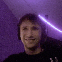 a man wearing headphones is smiling in a dark room with purple lights behind him