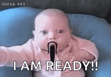 a baby with a pacifier in its mouth is sitting on a blue pillow and saying `` i am ready '' .