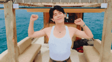 a man in a white tank top is flexing his muscles on a boat in the ocean