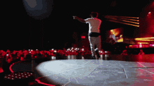 a man in a white shirt stands on a stage in front of a crowd of people