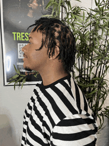 a man wearing a black and white striped shirt stands in front of a poster that says tres