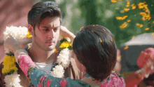 a woman is putting flowers on a man 's neck