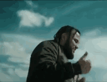 a man with a beard is giving a thumbs up while standing in front of a blue sky .