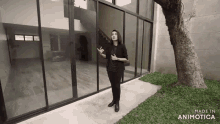 a woman is standing in front of a house with sliding glass doors and a tree .