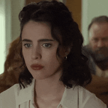 a close up of a woman 's face with a man behind her in the background