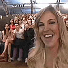 a woman is taking a selfie in front of a crowd of people sitting in chairs .