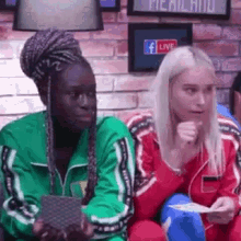 a black woman and a white woman are sitting next to each other on a couch and looking at something .