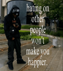 a man wearing a hoodie and a hat with the words hating on other people won 't make you happier written on it