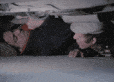 two men are looking underneath a car and one is wearing a hat