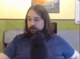 a man with long hair and a beard is sitting in front of a wall with a painting on it .