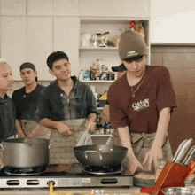 a man wearing a brown shirt that says zky is cooking in a kitchen