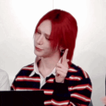 a person with red hair is wearing a striped shirt and making a gesture with their finger .
