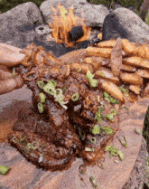 a steak and french fries on a wooden cutting board with a fire in the background