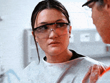 a woman wearing safety goggles looks at a man in a lab coat