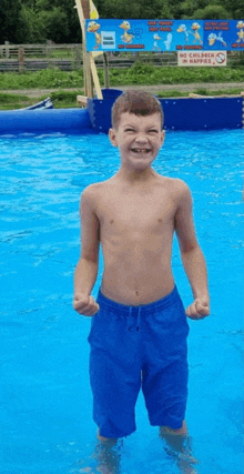 a young boy without a shirt is standing in a swimming pool and smiling .