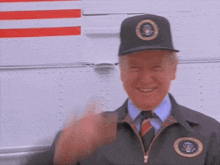 a man wearing a black hat with the presidential seal on it is smiling and waving