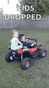 a boy and a girl are riding a toy truck in a yard .
