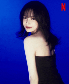 a woman in a black dress is standing in front of a blue background with the letter n in red