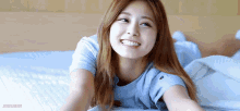 a woman in a blue shirt is laying on a bed smiling