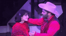 a man in a cowboy hat is hugging a woman in a red dress on stage .