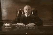 a man in a judge 's robe is sitting at a desk with a gavel .