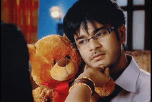 a man with glasses is holding a teddy bear with a red bow