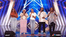 a group of people singing on a stage with a nbc logo in the corner