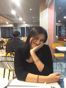 a woman sits at a table with her hand on her chin