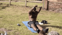 a shirtless man is laying on a yoga mat in the grass with his arms in the air