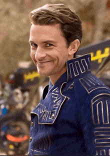 a man in a blue jacket with the letter e on the collar smiles