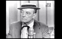a man in a suit and hat is talking into a microphone in a black and white photo .