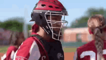 a softball player wearing a helmet and a catcher 's mask is talking to another player on the field .