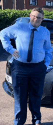 a man in a blue shirt and tie stands in front of a car