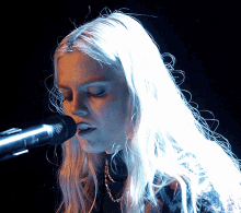 a woman singing into a microphone with her eyes closed
