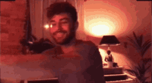 a man with a beard is smiling in front of a lamp in a dark room
