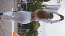 a woman in white pants stretches her arms in front of a building that says co