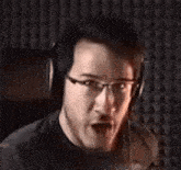 a man wearing glasses and headphones is sitting in front of a microphone and making a funny face .
