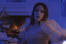 a woman in a white dress is sitting in front of a fireplace holding a string of lights