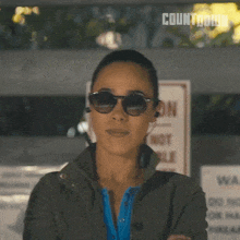 a woman wearing sunglasses stands with her arms crossed in front of a no parking sign