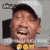 a man wearing a hat is crying with his eyes closed and the words aku terharu aku wak .