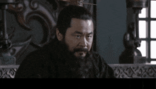 a man with a beard is sitting in front of a screen with chinese characters on it