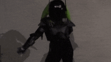 a person in a futuristic suit is standing in the dark with a green light behind them .