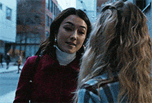 a woman in a red coat talks to another woman