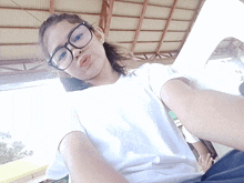 a girl wearing glasses and a white shirt is taking a picture of herself